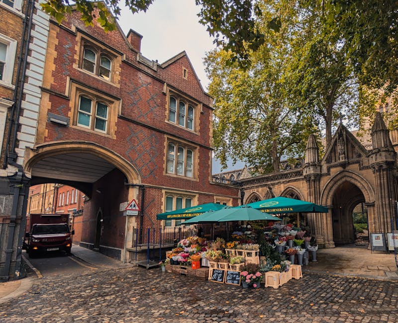A vibrant outdoor flower stall situated on a cobblestone street near St Albans Cathedral, featuring a variety of fresh flowers including roses, tulips, and seasonal blooms arranged in bouquets and sma